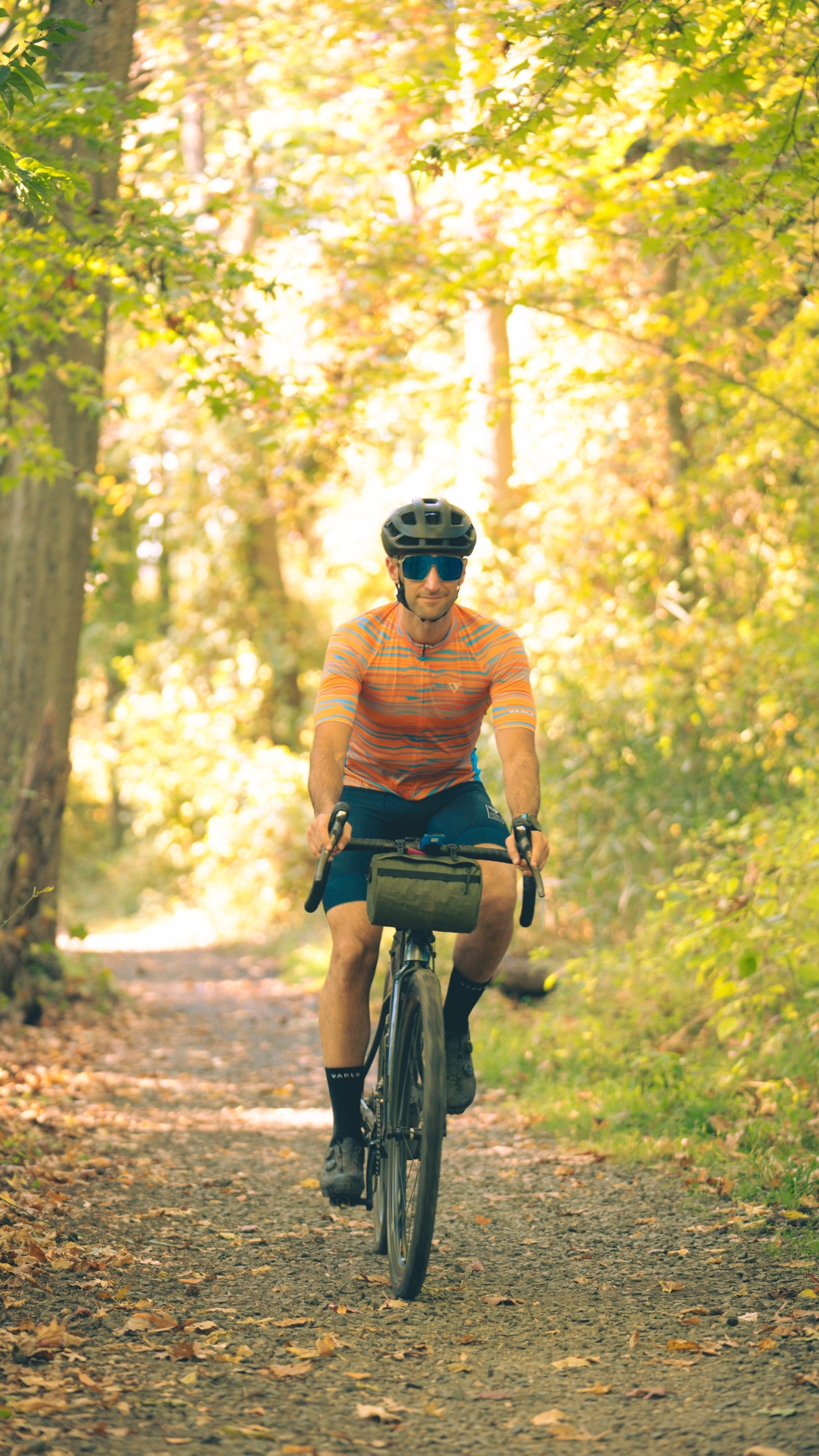 Male riding a bike off road as he sports the new pioneer gravel jersey in path orange from the Varlo 2025 gravel series.